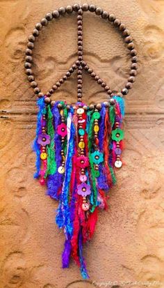 a peace sign made out of beads and other things hanging on a wall with the word peace written in it