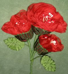 three red roses with green leaves on a gray surface, one is sewn and the other is sewn