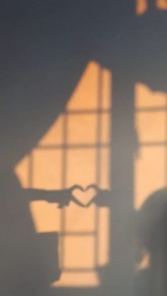 the shadow of a person making a heart shape with their hand in front of a window