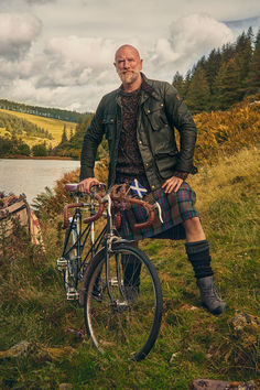 a man standing next to his bike on the side of a hill near a lake