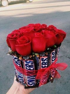 a hand holding a candy bar bouquet with roses in it's wrapper on the street