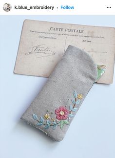 an old envelope with flowers on it is next to a small piece of cloth that has been embroidered onto