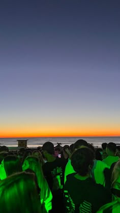 a group of people standing on top of a beach next to the ocean at sunset