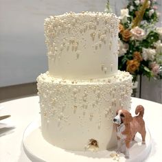 a three tiered cake with beading and a dog figurine on the side