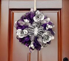 a purple and silver wreath hanging on the front door with flowers in it's center