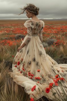 a woman in a long dress is standing in a field with red flowers and grass