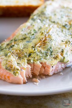 a piece of salmon on a white plate with bread in the background and a knife stuck into it