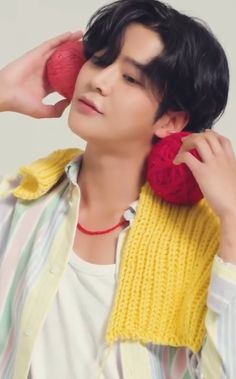 a young man holding an object to his ear while wearing a yellow and red sweater