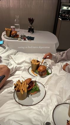 two people sitting at a table with plates of food in front of them, one holding a cell phone