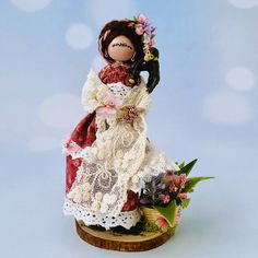 a doll is standing on a piece of wood with flowers in her hair and dress