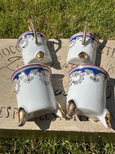 three white and blue vases sitting on top of a cement slab in the grass