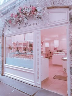 a store front with pink flowers hanging from it's glass door and windows on the outside