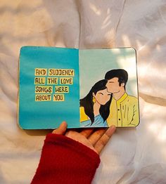 a hand holding a book with an image of a man kissing a woman