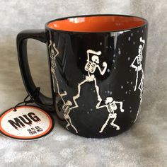 a black coffee mug with skeletons on it next to an orange and white sticker