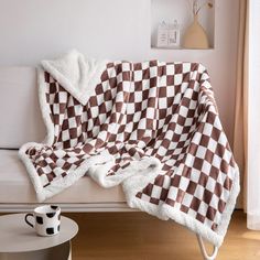 a couch covered with a checkered blanket and coffee mug on it's side