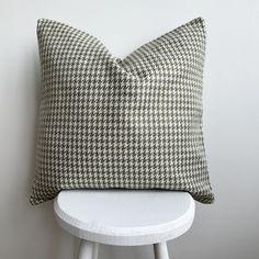 a green and white pillow sitting on top of a white stool next to a wall