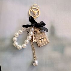 a key chain with a bottle of perfume on it and pearls attached to the lanyard