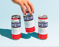 two cans of beer being held by a woman's hand and another can in the background