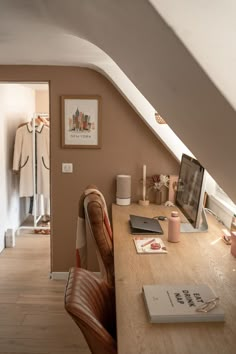 a desk with a computer and books on it next to a window in an attic