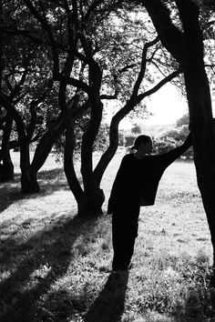 black and white photograph of man standing in front of trees with arms stretched out to the side