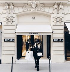 a woman walking past a chanel store with bags in her hand and the door open