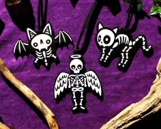 three halloween decorations on a purple cloth with bats and skulls hanging from it's sides