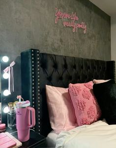 a black headboard with pink pillows and lights on the wall next to a bed