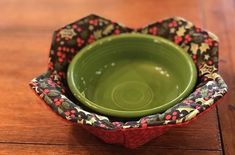 a green bowl sitting on top of a wooden table next to a black and red flowered napkin