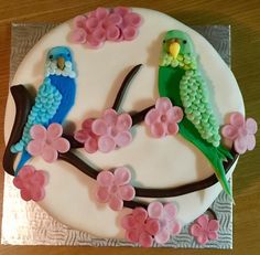 a decorated cake with two birds sitting on a tree branch and pink flowers in front of it