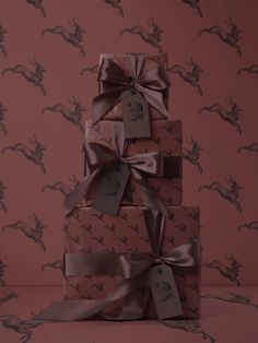 a stack of wrapped presents on top of a pink tablecloth covered with brown ribbon