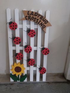 a white picket fence with ladybugs and sunflowers on it, attached to a sign that says ladybird crossing