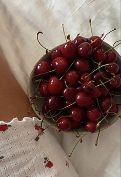 a bowl full of cherries sitting on top of a bed next to a woman's arm