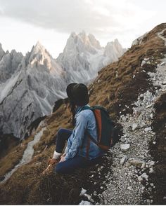 a person sitting on the side of a mountain looking at snow covered mountains in the distance