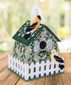 a small house made out of plastic beads on top of a wooden table with a tissue dispenser in front of it