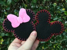 someone is holding two mickey mouse ears with pink and black bows on them in front of some bushes