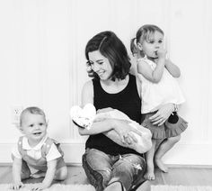 a woman sitting on the floor with two small children and one holding a stuffed animal