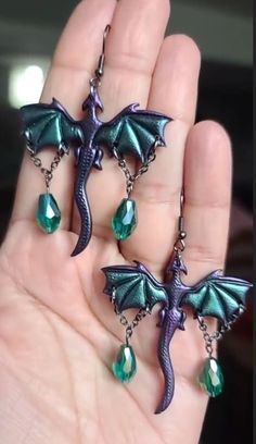 two dragon shaped earrings with green crystals hanging from them's earwires on a person's hand