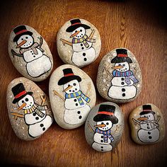 painted rocks with snowmen on them sitting on a wooden table next to each other