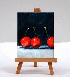 a painting of three cherries on an easel