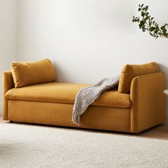 a yellow couch sitting on top of a white rug in a living room next to a plant