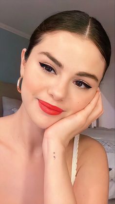 a woman with her hand on her chin, wearing red lipstick and looking at the camera