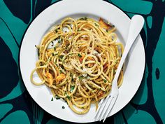 a white plate topped with pasta on top of a blue and green table cloth next to a fork