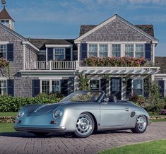 a silver sports car parked in front of a large house with flowers on the roof