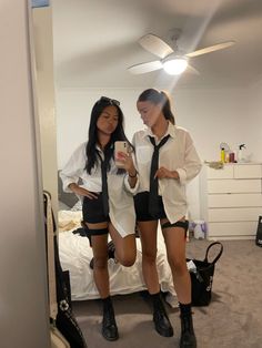 two young women standing in front of a bed looking at their cell phones while wearing short shorts