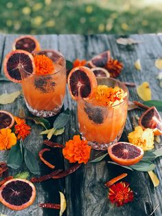 two glasses filled with blood orange juice and garnished with flowers on an old wooden table