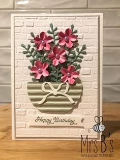 a birthday card with flowers in a vase on top of a wooden table next to a brick wall