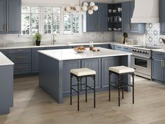 a kitchen with blue cabinets and white counter tops, two stools in front of the island