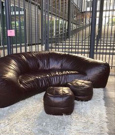 a brown leather couch sitting on top of a white rug next to a metal fence