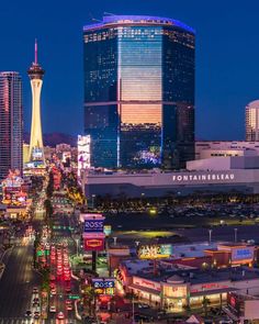 the city skyline is lit up at night with lights on and tall buildings in the background