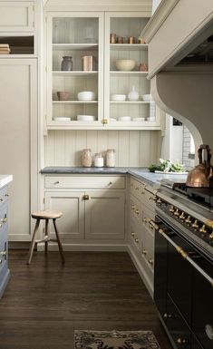 a kitchen with white cabinets and gold knobs on the stove top, along with a wooden stool